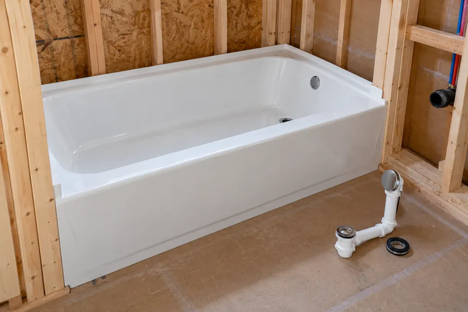 Bathtub in a renovation area with drain and overflow components nearby.